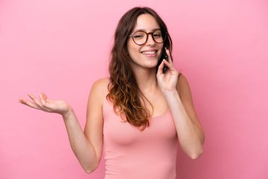 Pembe arka planda izole edilmiş genç beyaz bir kadın cep telefonuyla sohbet ediyor.