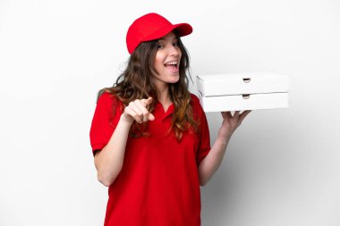 İş üniformalı pizzacı kadın beyaz arka planda izole edilmiş pizza kutuları alıyor şaşırmış ve ön tarafı işaret ediyor.