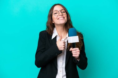 Genç TV sunucusu, mavi arka planda izole edilmiş bir kadın baş parmak hareketi yapıyor.