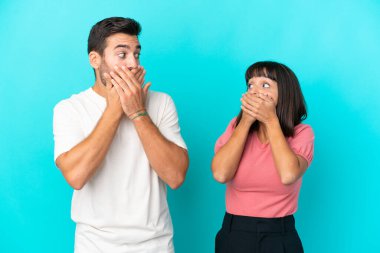 Young couple isolated on blue background covering mouth with hands for saying something inappropriate