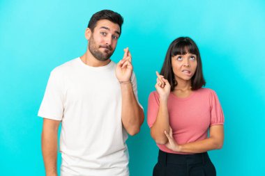 Mavi arka planda izole edilmiş genç bir çift parmaklarını çapraz yapıp en iyisini diliyor.