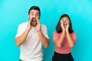 Genç çift mavi arka planda izole edilmiş bağırıyor ve bir şey duyuruyor.