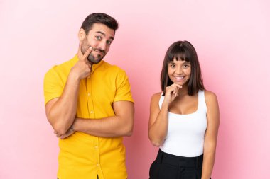 Pembe arka planda yalnız yaşayan genç bir çift tatlı bir ifadeyle gülümsüyor.