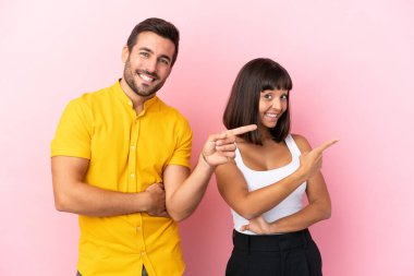 Pembe arka planda izole edilmiş genç çift yan pozisyonda parmağı işaret ediyor.