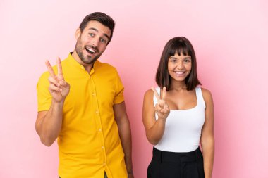 Pembe arka planda izole edilmiş genç çift gülümsüyor ve zafer işareti gösteriyor.