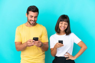 Mavi arkaplanda izole edilmiş genç bir çift cep telefonuyla bir mesaj ya da e-posta gönderiyor