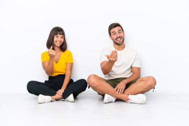 Yerde oturan genç çift beyaz arka planda soyutlanmış bir şekilde el ele gelmeye davet ediyorlar. Gelmene sevindim.