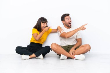 Yerde oturan genç çift, beyaz arka planda izole edilmiş bir şekilde bir fikir sunuyor ve gülümsüyor.