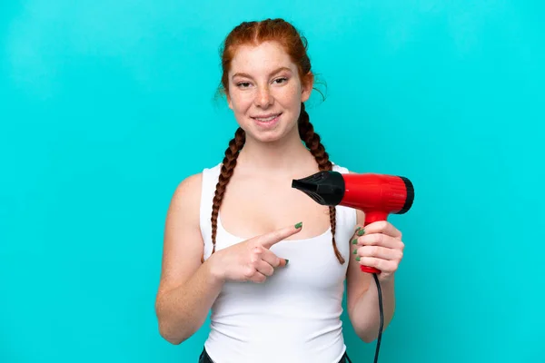 Young Caucasian Reddish Holding Hairdryer Isolated Blue Background Pointing — Foto Stock