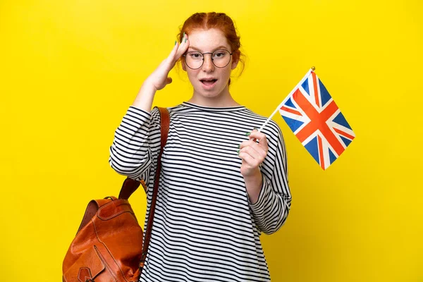 Young hispanic woman holding an United Kingdom flag isolated on yellow background with surprise expression