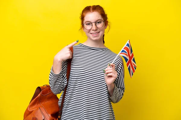 Young hispanic woman holding an United Kingdom flag isolated on yellow background giving a thumbs up gesture