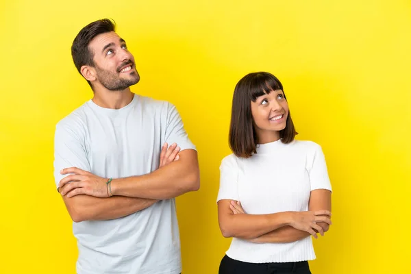 Young couple isolated on yellow background looking up while smiling