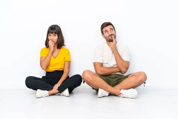 Jovem Casal Sentado Chão Isolado Fundo Branco Com Dúvidas Olhar — Fotografia de Stock