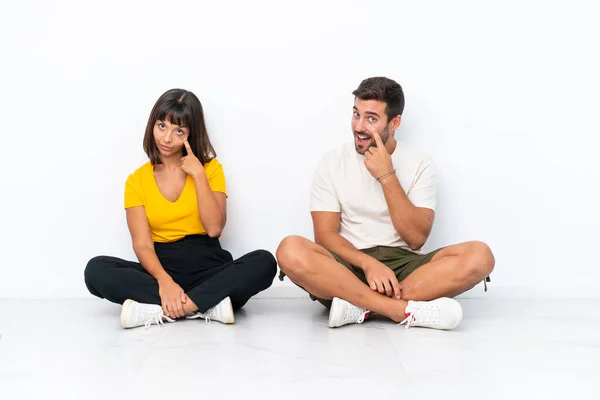 Young Couple Sitting Floor Isolated White Background Looking Front — Φωτογραφία Αρχείου