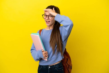 Student kid woman over isolated yellow background doing surprise gesture while looking to the side
