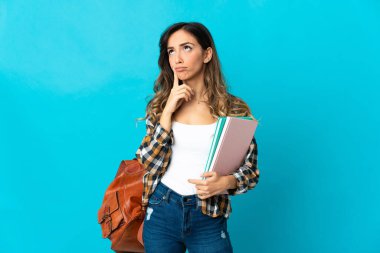 Genç bayan öğrenci, mavi arka planda izole edilmiş, yukarı bakarken şüphe duyuyor.