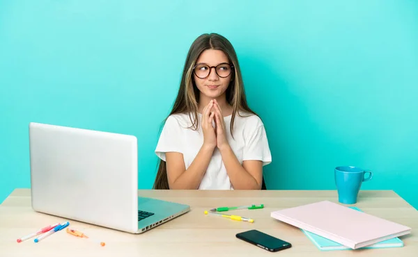 Little girl in a table with a laptop over isolated blue background scheming something