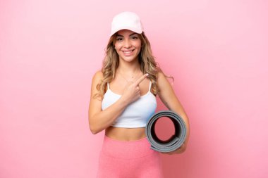 Genç sporcu kadın yoga derslerine giderken elinde bir hasırla ürünü sunuyor.