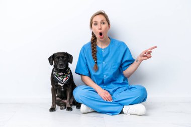 Beyaz arka planda izole edilmiş yerde köpeği olan genç bir veteriner kadın şaşırmış ve işaret ediyor.