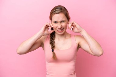 Pembe arka planda izole edilmiş genç beyaz kadın hayal kırıklığına uğramış ve kulaklarını kapatmış.