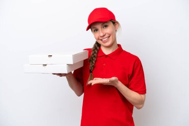 İş üniformalı bir pizzacı kadın beyaz arka planda izole edilmiş pizza kutuları alıyor. Davet etmek için ellerini yana uzatıyor.