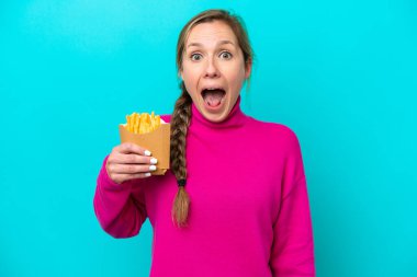 Mavi arka planda kızarmış patates kızartması tutan beyaz bir kadın. Şaşırtıcı bir yüz ifadesi var.
