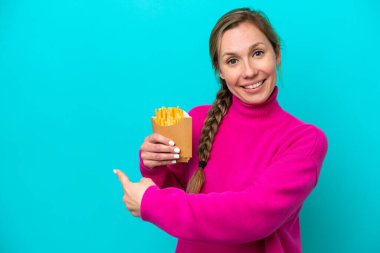 Elinde kızarmış cips tutan beyaz bir kadın mavi arka planda izole edilmiş.