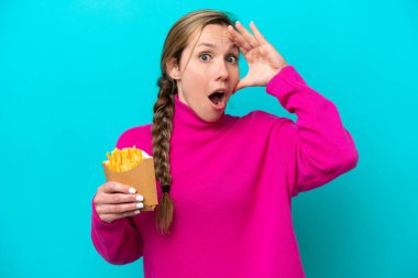 Kafkasyalı genç bir kadın elinde kızarmış cipslerle mavi arka plandan izole edilmiş bir şekilde yan tarafa bakarken sürpriz jest yapıyor.