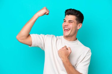 Genç, yakışıklı, beyaz bir adam mavi bir bakkalda izole edilmiş bir şekilde zaferi kutluyor.