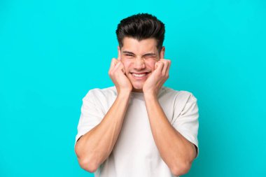 Genç, yakışıklı, beyaz bir adam mavi fırında izole edilmiş hayal kırıklığına uğramış ve kulaklarını kapatmış.