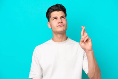 Genç, yakışıklı, beyaz bir adam, mavi fırında izole edilmiş, parmaklarını çapraz yapıp, en iyisini diliyor.