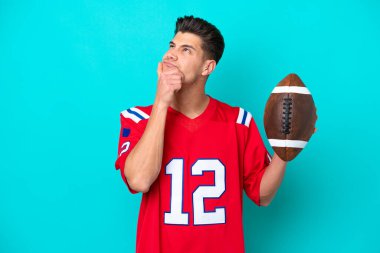 Rugby oynayan Kafkasyalı genç adam mavi arka planda izole edilmiş. Şüpheleri var.