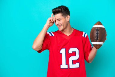 Rugby oynayan Kafkasyalı genç adam mavi arka planda izole bir şekilde gülüyor.