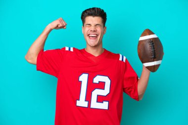 Genç beyaz adam rugby oynuyor. Mavi arka planda izole edilmiş. Güçlü bir hareket yapıyor.