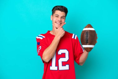 Rugby oynayan genç beyaz adam mavi arka planda izole edilmiş mutlu ve gülümsüyor.