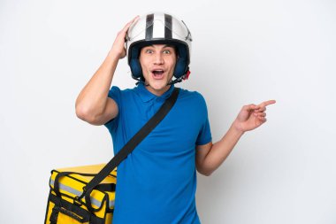 Beyaz arka planda izole edilmiş termal sırt çantalı beyaz bir adam şaşırmış ve parmağını kenarı işaret ediyor.