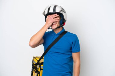 Beyaz arka planda izole edilmiş termal sırt çantalı beyaz tenli genç beyaz bir adam. Gözleri elleriyle kaplıyor ve gülümsüyor.