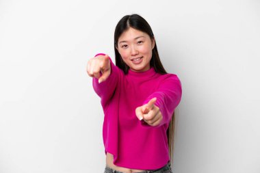 Beyaz arka planda izole edilmiş genç Çinli bir kadın mutlu bir ifadeyle ön tarafı işaret ediyor.