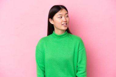 Young Chinese woman isolated on pink background looking to the side and smiling