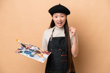 Genç Çinli ressam kadın bej arka planda izole edilmiş galibiyeti kutluyor.