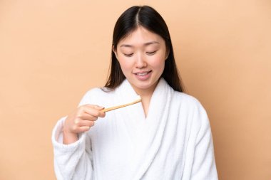 Bej arka planda diş fırçasıyla izole edilmiş genç bir Çinli kadın.