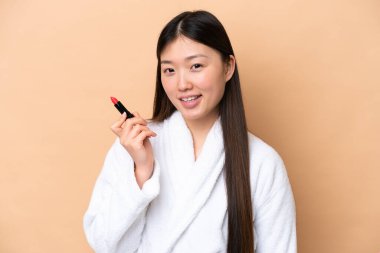 Young Chinese woman isolated on beige background holding red lipstick