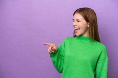 Mor arka planda izole edilmiş genç bir İngiliz kadın parmak göstererek bir ürün sunuyor.