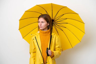 Young English woman with rainproof coat and umbrella isolated on white background looking to the side