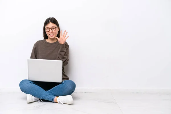 一个拿着笔记本电脑的年轻女人坐在地板上 用手指数着5 — 图库照片