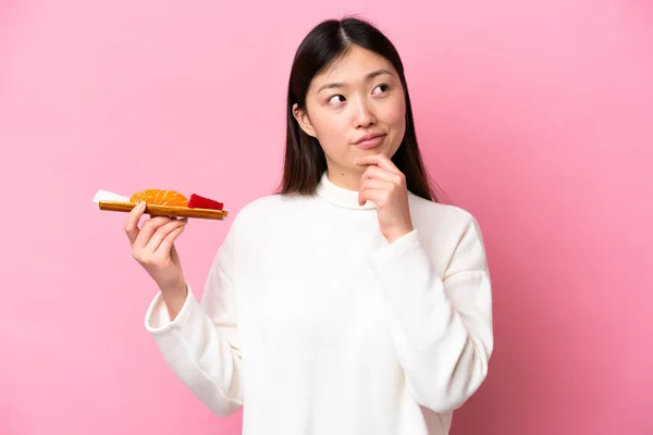 Young Chinese Woman Holding Sashimi Isolated Pink Background Looking — стоковое фото