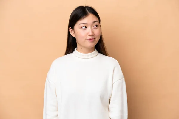 Young Chinese Woman Isolated Beige Background Making Doubts Gesture Looking — Φωτογραφία Αρχείου