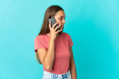 İzole edilmiş mavi arka planı olan genç bir kadın cep telefonuyla sohbet ediyor.