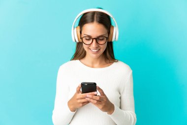 Soyutlanmış mavi arka plan müzik dinleyen ve cep telefonu arayan genç bir kadın.