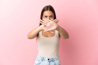 Soyutlanmış pembe arka planı olan genç bir kadın bir hareketi durdurmak için eliyle jest yapıyor.
